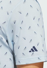 Svijetloplava atletska majica s teksturiranim uzorkom tamnoplavih trokuta i točkastim detaljima. Ima Adidas logo na rukavu.