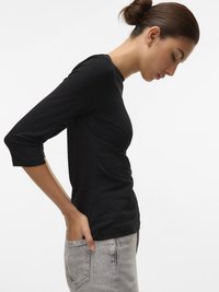 Svart tettsittende langermet topp laget av glatt stoff, med rund halslinning og en sidelomme. Kombinert med slitte grå jeans.
