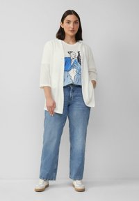Weißer Cardigan mit offener Vorderseite, getragen über einem grafischen T-Shirt mit blauer Illustration, kombiniert mit hellblauen geraden Jeans und weißen Sneakers.