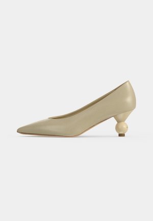 Escarpin beige à bout pointu avec un talon sculptural arrondi unique et une finition lisse, présenté sur un fond clair uni.