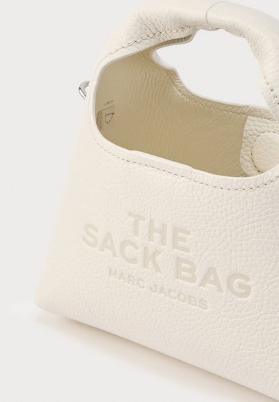Λευκή τσάντα χειρός από δερματίνη με υφή, με στρογγυλή λαβή στο επάνω μέρος, διαθέτει ανάγλυφη επιγραφή: "THE SACK BAG" και "MARC JACOBS" στην πρόσοψη.
