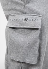 Grijze sportbroek van een textuurstof, met een grote zak met een klep en het "GORILLA WEAR" logo erop gedrukt.
