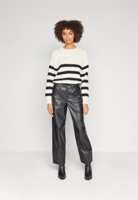 Suéter de punto en crema con rayas horizontales negras, combinado con pantalones anchos de cuero negro de talle alto y botines negros de tacón.