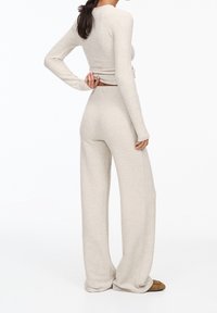 Haut à manches longues en maille beige clair et pantalon large assorti, présentant une texture douce et une taille ajustée, avec un design minimaliste.