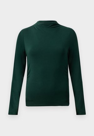 Sötétzöld, hosszú ujjú, könnyű felső, álló gallérral és testhez simuló szabással, sima világos háttér előtt.