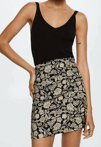 Top sin mangas de canalé negro con tirantes ajustables, combinado con una falda corta de patrón floral en negro y beige, que presenta una abertura lateral.