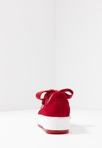 Zapatillas de gamuza roja con suela texturada blanca, con una forma redondeada y cordones a juego atados en la parte trasera. Diseño limpio sin marcas visibles.