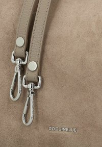 Sac à main en suédine beige avec des anses en cuir texturé, des clips métalliques et un logo. Présente une surface lisse et un fini doux et mat.