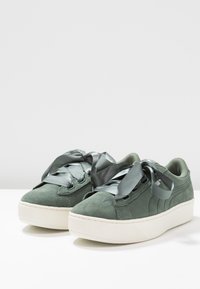 Grüne Wildleder-Sneaker mit einer weißen Gummisohle und Plateau, ausgestattet mit satinschwarzen Schnürsenkeln und einem strukturierten Design an Obermaterial und Sohle.