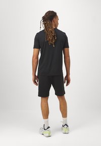 Camiseta negra de manga corta y pantalones cortos negros, combinados con zapatillas grises y lima, vista desde atrás, mostrando un ajuste relajado.