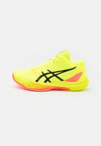 Zapatilla deportiva de color amarillo brillante con detalles en negro y malla. Cuenta con una suela acolchada con toques de color rosa y un cierre de cordones seguro.