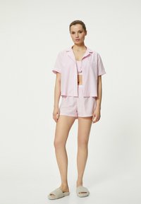 Conjunto de pijama de manga corta a rayas rosa y blanca con una camiseta de botones y pantalones cortos, hecho de tela ligera; unas pantuflas cómodas completan el atuendo.