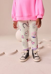 Leggings bianchi a coste con stampe floreali colorate e arcobaleno, abbinati a sneakers nere alte e una felpa oversize rosa.