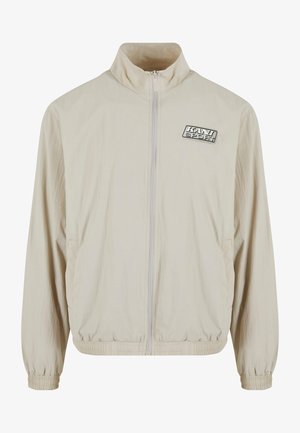 Beige lichtgewicht jack met een hoge kraag, volle rits, elastische boorden en onderkant. Bevat een logopatch op de linker borst en zijzakken.