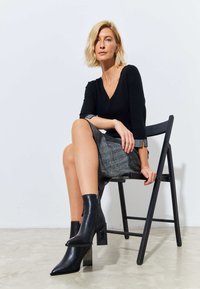 Maglione aderente nero con scollo a V, abbinato a una gonna grigia con texture. Il modello indossa stivaletti neri a punta con tacco quadrato spesso.