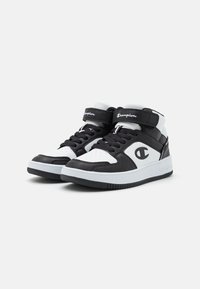Sorte og hvite høy-top sneakers med lær og tekstilmateriale, snøring, stroppelukking og logo-detalj på siden.