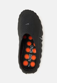 Μαύρο παπούτσι τύπου slip-on με διάτρητο επάνω μέρος, στρογγυλεμένες άκρες και υφή στη σόλα. Το εσωτερικό διαθέτει πορτοκαλί μαξιλαράκια με κουκκίδες και λογότυπο.