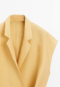 Hellgelbe ärmellose Blazerjacke mit breiten Revers und strukturierten Schultern, auf weißem Hintergrund dargestellt.