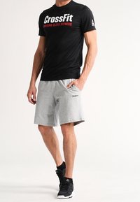 Černé sportovní tričko s bílým a červeným logem "CrossFit", doplněné šedými šortkami a černými teniskami s texturovanou podrážkou.