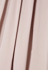 Jupe plissée en tissu rose pastel doux. Présente une texture lisse et des drapés fluides. Aucune ornementation ni matériel visible.