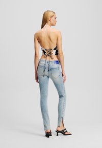Černobílý crop top bez zad se šněrováním a háčkovaným vzorem. Spárován s světle modrými džínami s bočními rozparky.