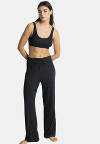 Soutien-gorge de sport noir côtelé avec larges bretelles, associé à un pantalon noir à taille élastique et coupe ample avec une surface texturée.
