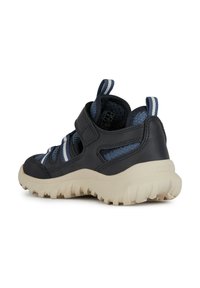 Zapatillas deportivas de color azul oscuro, hechas de material de malla y goma, con una correa de velcro y una suela texturizada de color beige para proporcionar tracción.