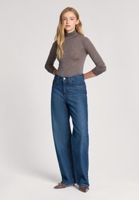 Maglietta grigia a collo alto aderente abbinata a jeans in denim blu a vita alta e gamba larga. I pantaloni presentano un classico design a cinque tasche.