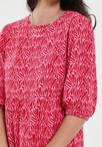Vestido corto de manga corta en rojo y rosa con un patrón de cebra, con un escote redondo y cintura fruncida para un detalle adicional.