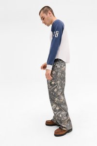 Langsleeve shirt met een witte romp en blauwe mouwen, met een graphic op de linkerarm. Gepatchte, gestructureerde grijze broek en bruine schoenen.