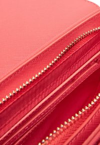 Portefeuille texturé rouge présentant plusieurs compartiments, zips en ton doré et doublure intérieure lisse, mettant en valeur des éléments de design fonctionnel.