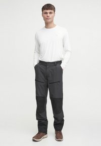 Pantalones exteriores negros con bolsillos con cremallera, tela duradera y acentos de panel texturizado en negro. Combinados con una camisa blanca de mangalarga.