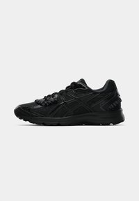 Baskets de sport noires avec une surface texturée, des motifs de points subtils et un logo réfléchissant. Caractéristiques d'une semelle rembourrée et d'un design à lacets.
