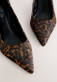Décolleté con tacco a punta stampa leopardata, con tomaia marrone e nera dalla texture, e interno lucido nero. Design elegante e moderno.