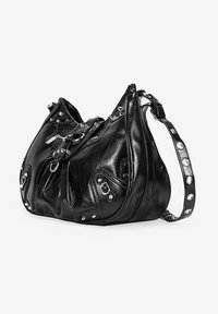 Bolso de cuero negro con un diseño relajado. Presenta herrajes metálicos y tachuelas, una superficie texturizada y una correa ancha con acentos circulares.