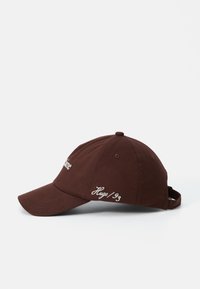 Brown cotton baseball cap with an adjustable strap, featuring white embroidered text on the front and side. Smooth texture, rounded brim.