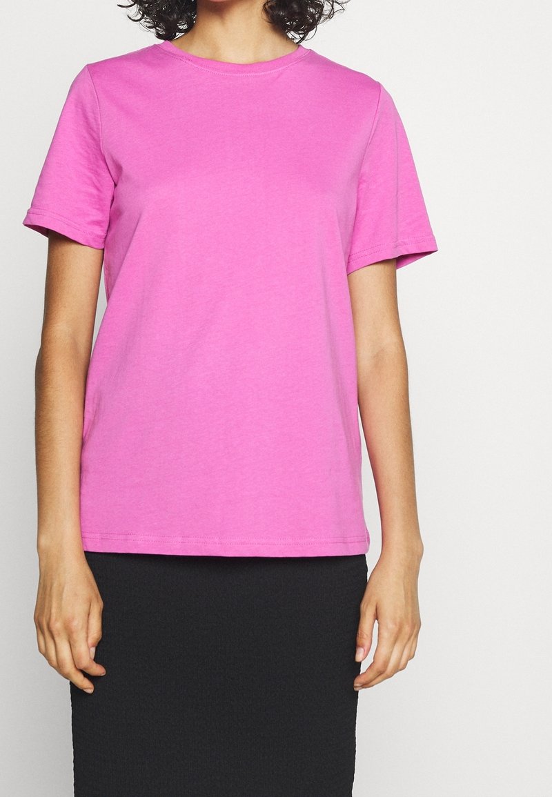 Růžové bavlněné tričko s krátkým rukávem, kulatým výstřihem a hladkou texturou. Nošeno s černou sukní, která má jednoduchý design a střih.