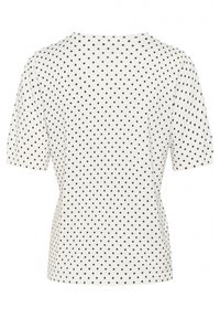 Haut à manches courtes en tissu blanc avec des pois noirs, doté d'un col rond et d'une silhouette ajustée, fabriqué en matériau doux et extensible.