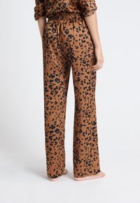 Pantalones de pierna ancha en estampado de leopardo en un tejido marrón, con una cinturilla elástica fruncida y una textura suave y ligera.