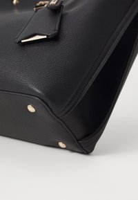 Sort læderhåndtaske med struktureret finish. Har guldfarvet hardware, skarpe kanter og beskyttende metalfødder i bunden.