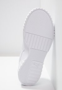 Suela de zapatilla atlética blanca con superficie de goma texturizada, que presenta ranuras verticales y horizontales. Detalle del logo cerca del talón.
