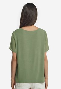 Grön kortärmad topp med rund halsringning och slät yta, med en lös passform. Baksidan är enkel med diskreta axeldetaljer.