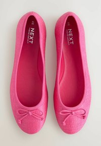 Helle rosa Ballerinas aus strukturiertem Stoff, mit einer abgerundeten Spitze und einem dekorativen Schleifenakzent auf der Vorderseite.