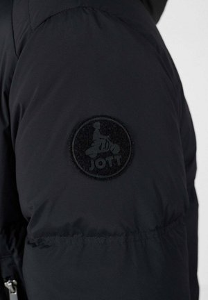 Chaqueta de plumas negra con un parche circular texturizado con un logotipo en la parte superior del brazo. La tela parece suave e insulated.