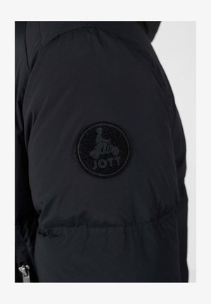 Schwarze Steppjacke mit einem runden, strukturierten Aufnäher mit Logo am Oberarm. Der Stoff wirkt glatt und isoliert.