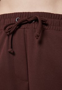 Bruna sweatsbyxor har en elastisk midjeband med dragsko, sidoficka och mjuk textur. Fokuserar på komfort och avslappnade designelement.