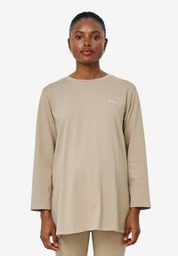 Beige Langarmshirt mit Rundhalsausschnitt und lockerer Passform. Verfügt über ein kleines weißes "Amour"-Logo auf der linken Brust. Glattes Stoffgefühl.