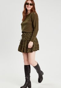 Olive green sweater with button accents, paired with a black and gold leopard-print tiered mini skirt. Finished with knee-high black boots.
