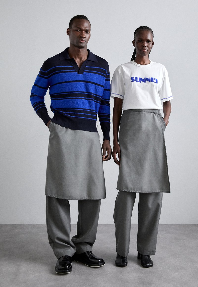 Maglione a righe blu e navy, gonne grigie e pantaloni a gamba larga. Scarpe nere con texture liscia e design formale.