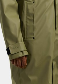 Olivengrøn vandtæt jakke med glat tekstur, lange ærmer, justerbar manchet med velcro og en sidelomme.